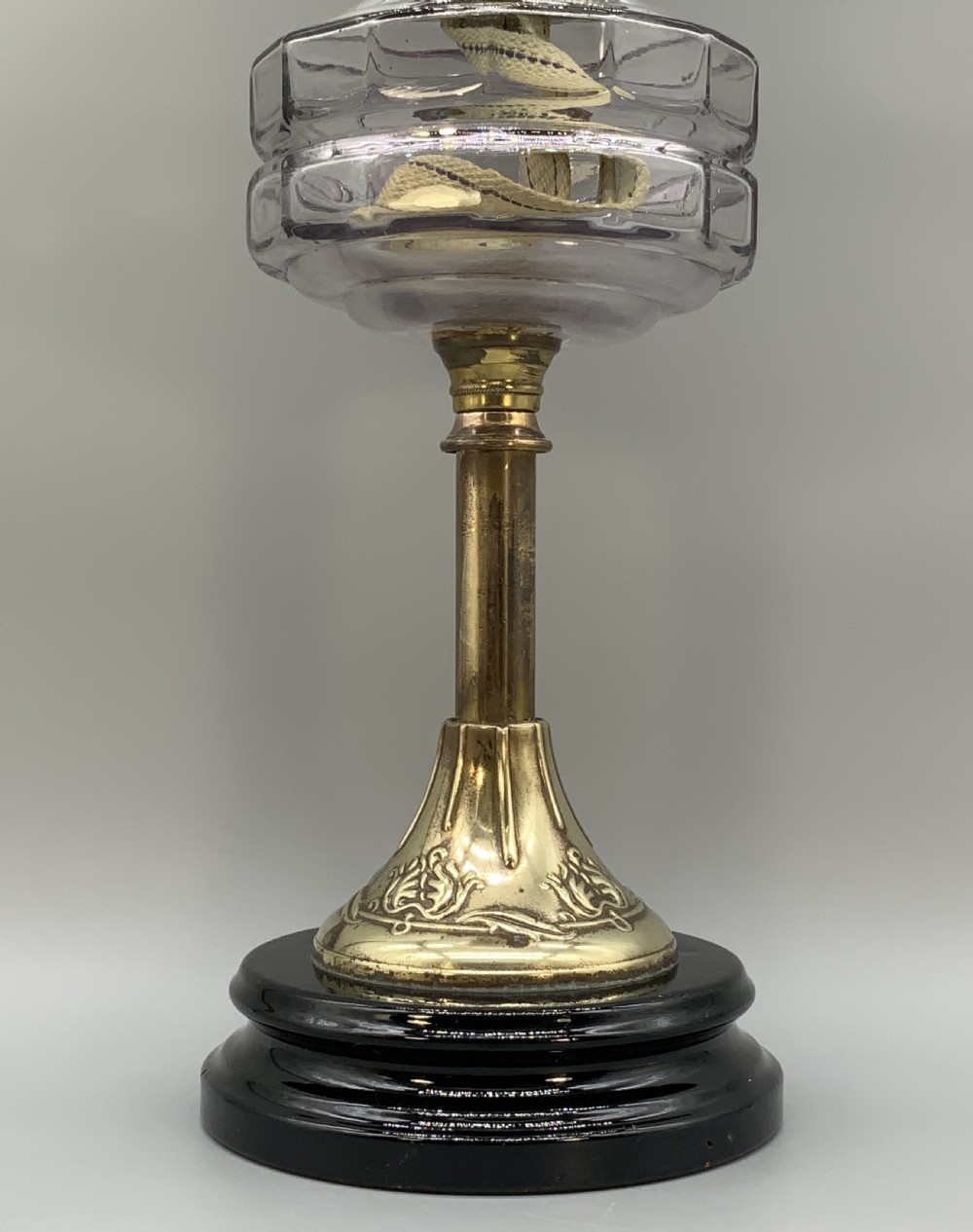 An Art Nouveau table oil lamp featuring a black ceramic base, cast brass stem, clear glass reservoir, double wick burner, clear chimney, and ruffled glass shade. View VI