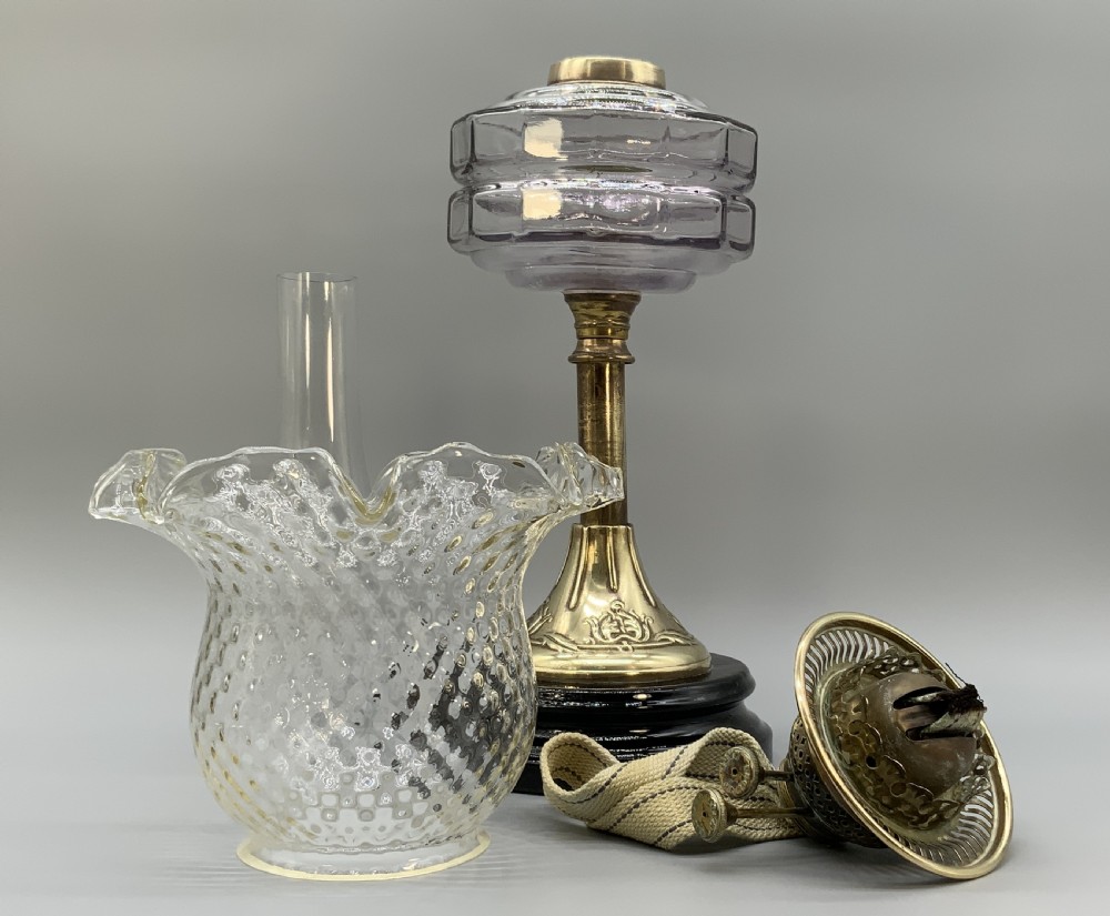 An Art Nouveau table oil lamp featuring a black ceramic base, cast brass stem, clear glass reservoir, double wick burner, clear chimney, and ruffled glass shade. View XII