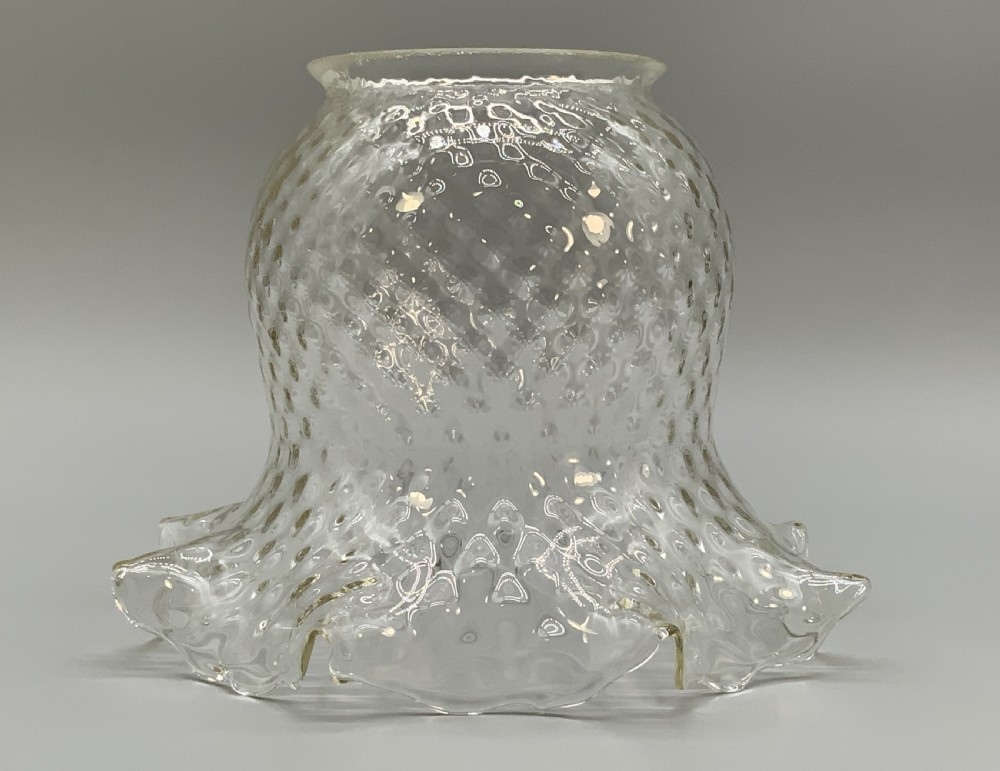 An Art Nouveau table oil lamp featuring a black ceramic base, cast brass stem, clear glass reservoir, double wick burner, clear chimney, and ruffled glass shade. View XV