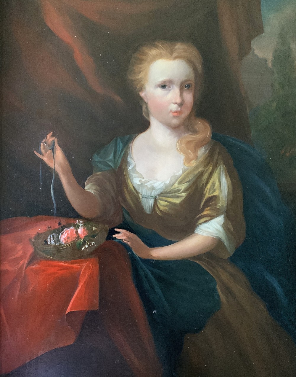 An antique oil painting depicting a seated woman beside a basket of flowers on a draped table, set within a gilded wooden frame. View V