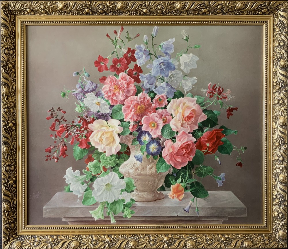 A framed oleograph print depicting a bouquet of pink, red, and blue garden flowers in an ornate ceramic urn on a stone ledge, enclosed within a decorative gilded frame.