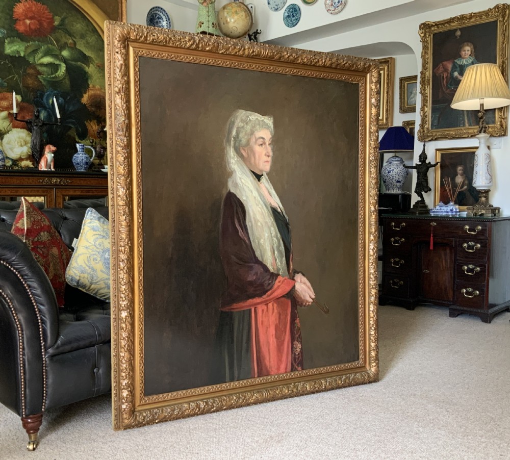 A large framed oil portrait painting on canvas depicting a mature woman wearing a lace head covering and draped red shawl against a dark brown background. View III