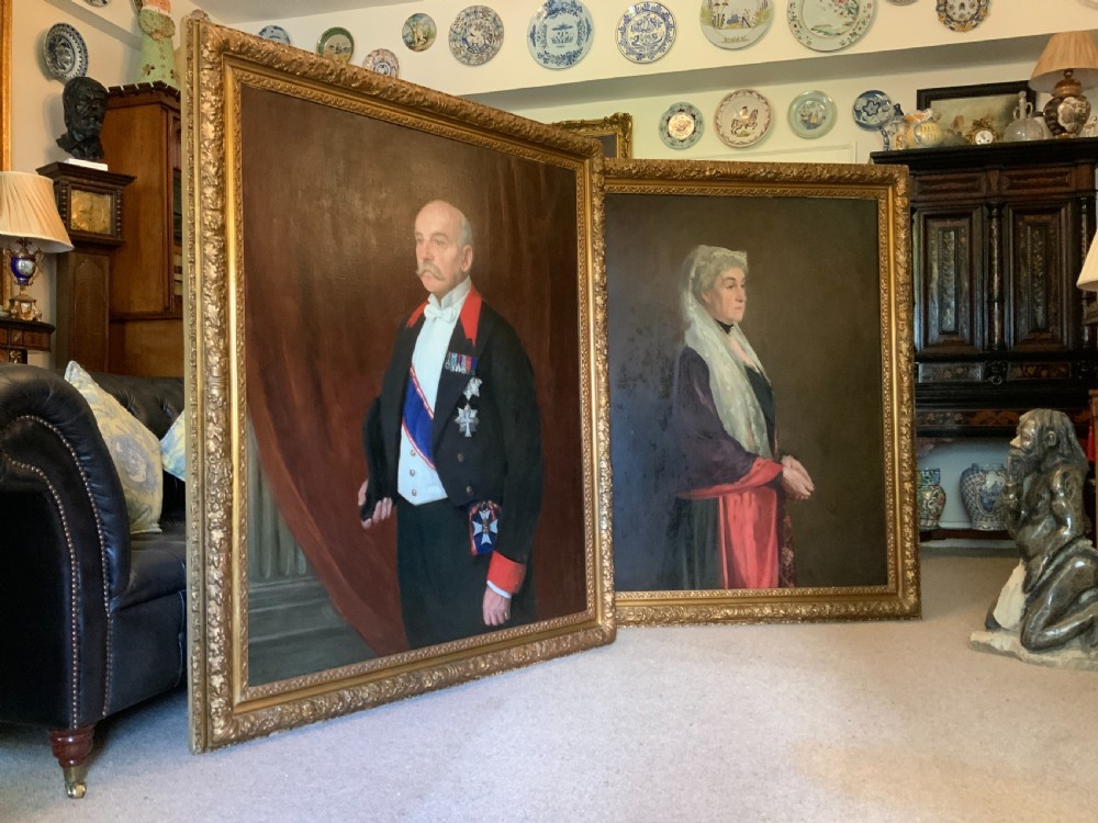 A large framed oil portrait painting on canvas depicting a mature woman wearing a lace head covering and draped red shawl against a dark brown background. View X