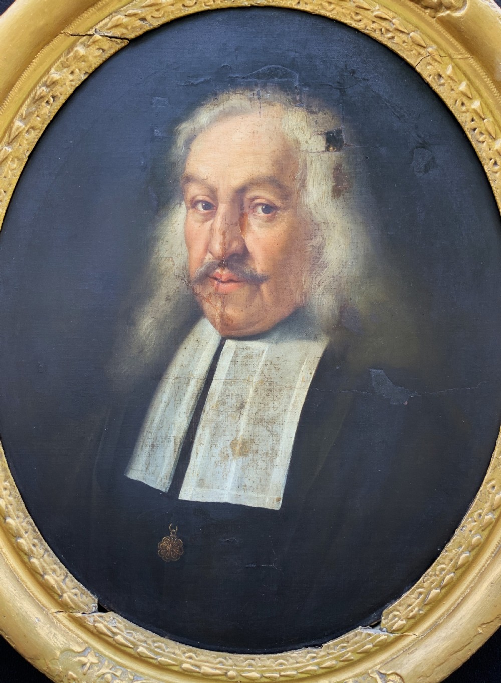 A seventeenth-century oval oil portrait of a gentleman with grey hair wearing a black coat and white collar, housed in a carved gold leaf frame. View II