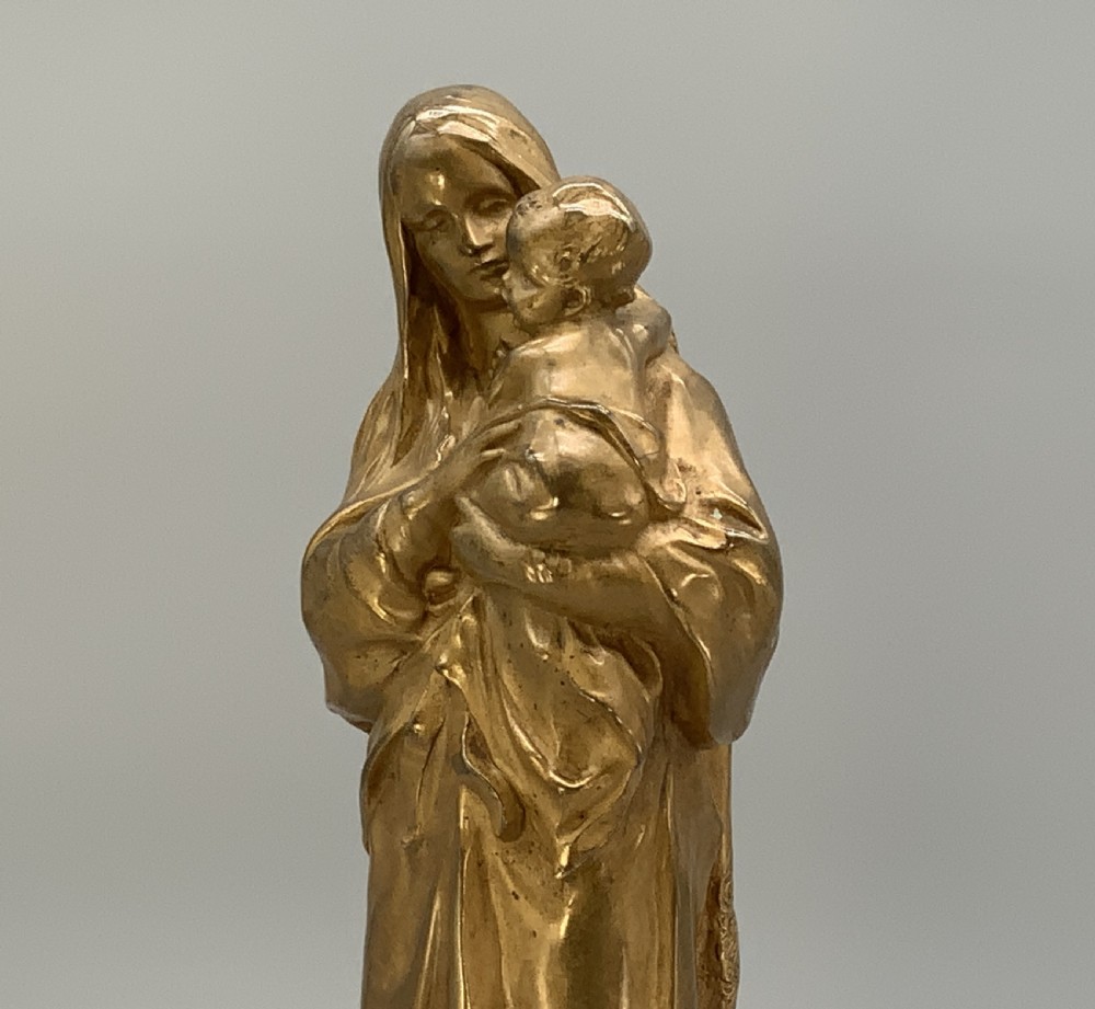 A gilt bronze sculpture depicting the Madonna holding the infant Christ, mounted on a square dark green marbled base. View XI