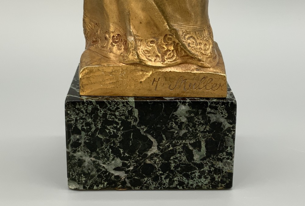 A gilt bronze sculpture depicting the Madonna holding the infant Christ, mounted on a square dark green marbled base. View XII