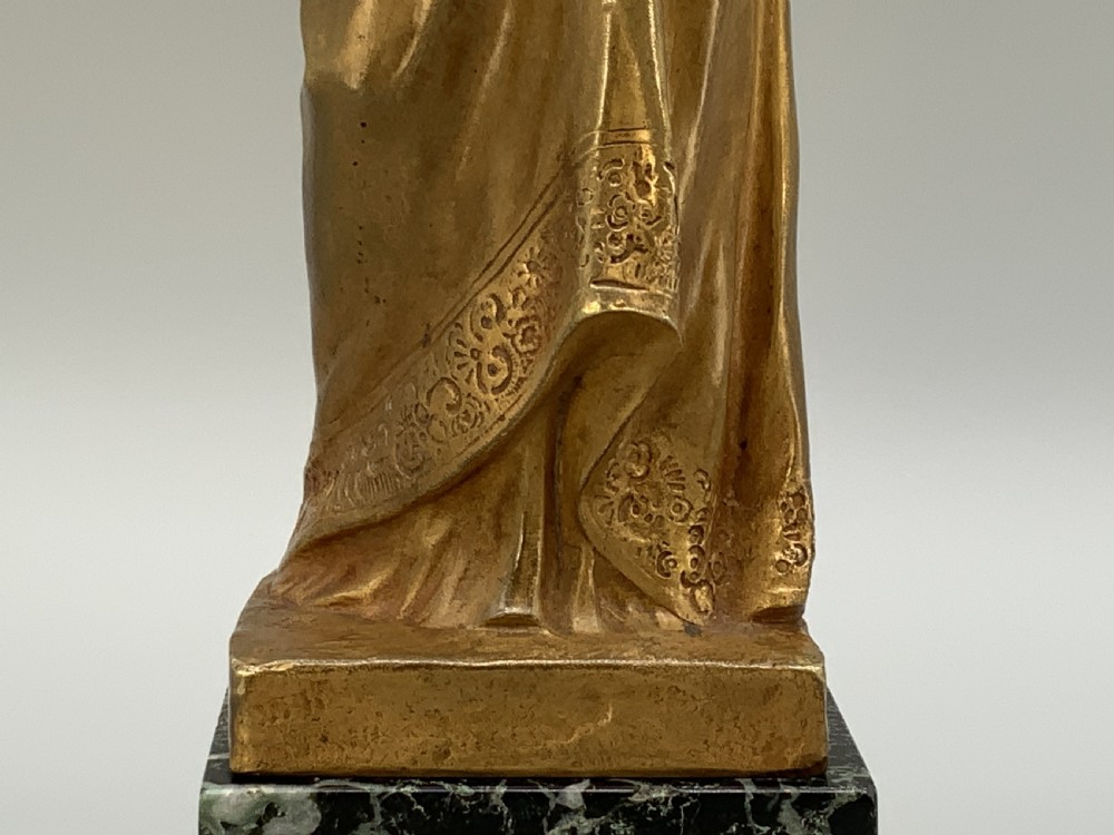 A gilt bronze sculpture depicting the Madonna holding the infant Christ, mounted on a square dark green marbled base. View XIV