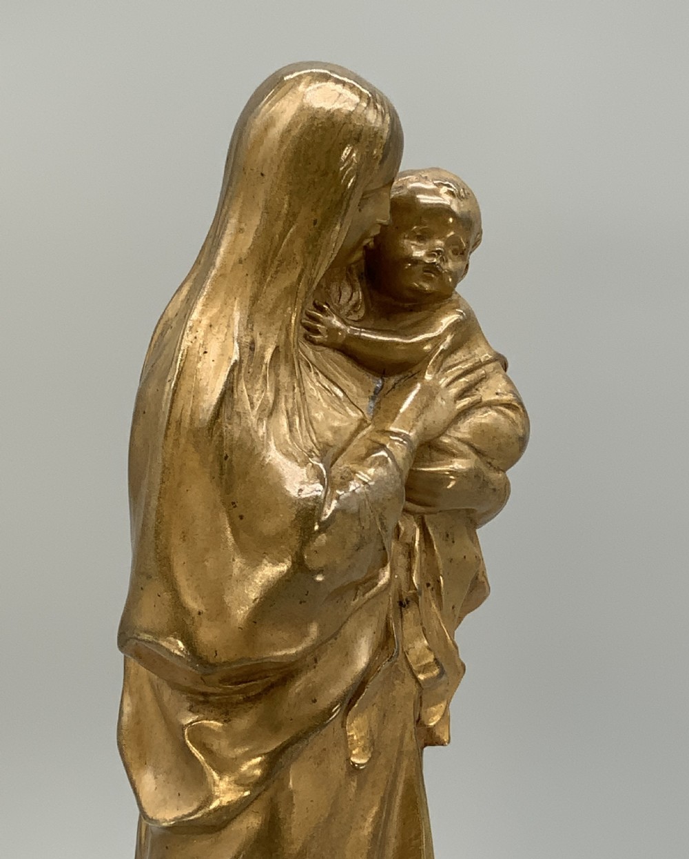 A gilt bronze sculpture depicting the Madonna holding the infant Christ, mounted on a square dark green marbled base. View XV