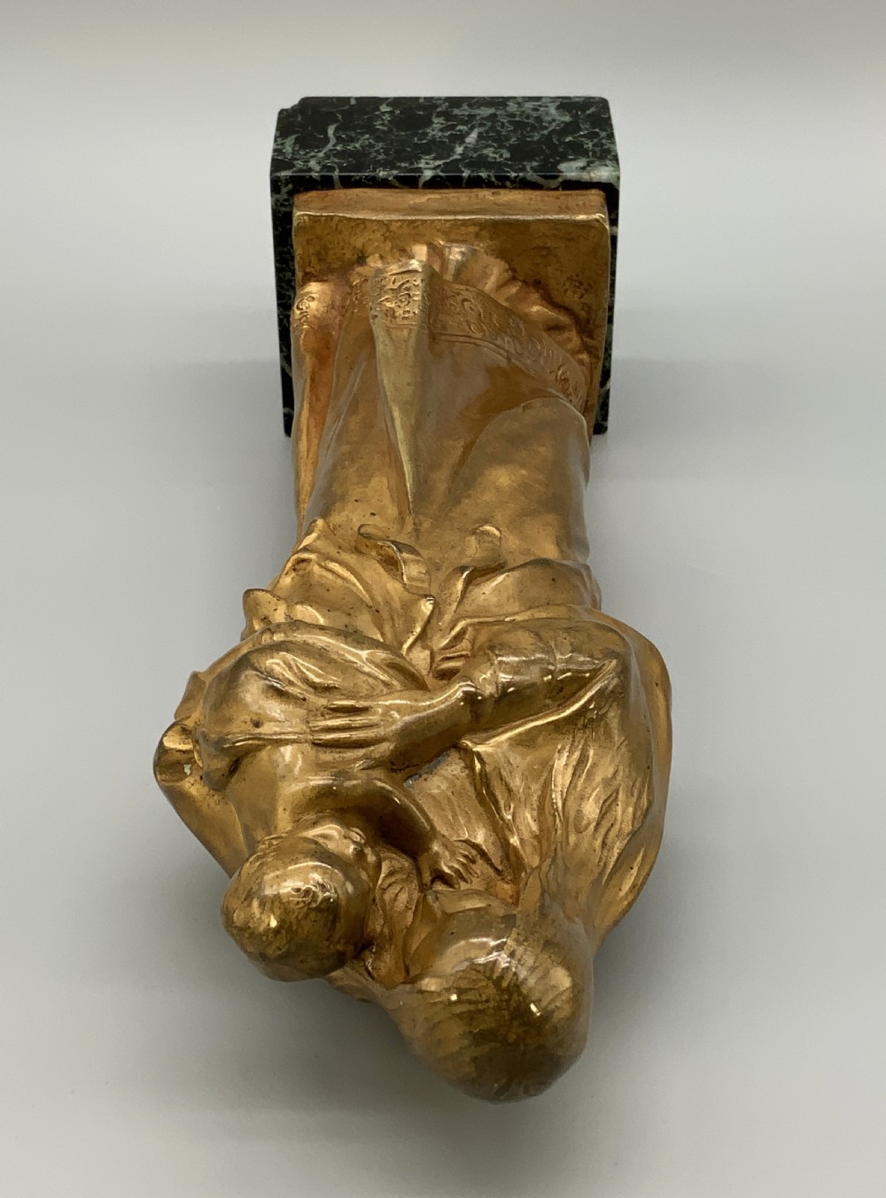 A gilt bronze sculpture depicting the Madonna holding the infant Christ, mounted on a square dark green marbled base. View XVI