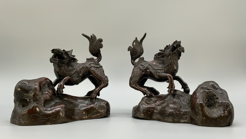 A pair of patinated dark bronze Japanese mythical creature statues positioned on sculpted rocky bases.