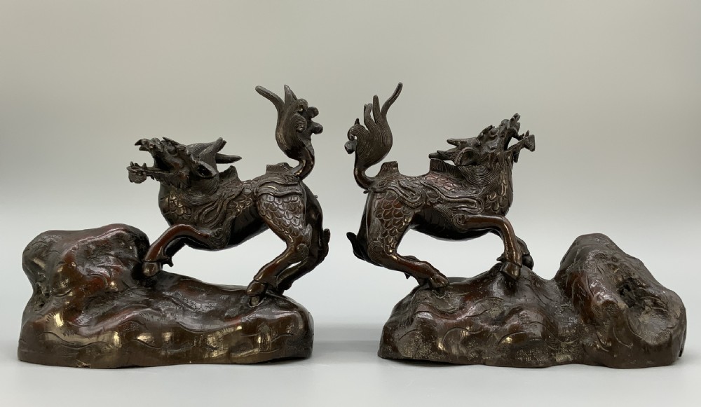 A pair of patinated dark bronze Japanese mythical creature statues positioned on sculpted rocky bases. View IV