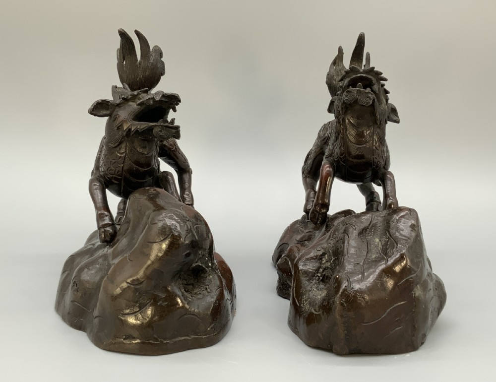 A pair of patinated dark bronze Japanese mythical creature statues positioned on sculpted rocky bases. View X