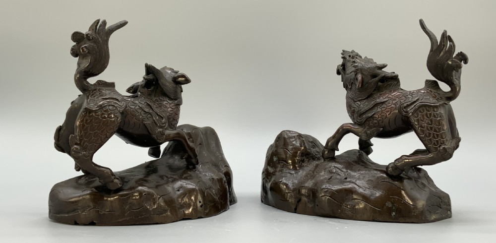 A pair of patinated dark bronze Japanese mythical creature statues positioned on sculpted rocky bases. View XII