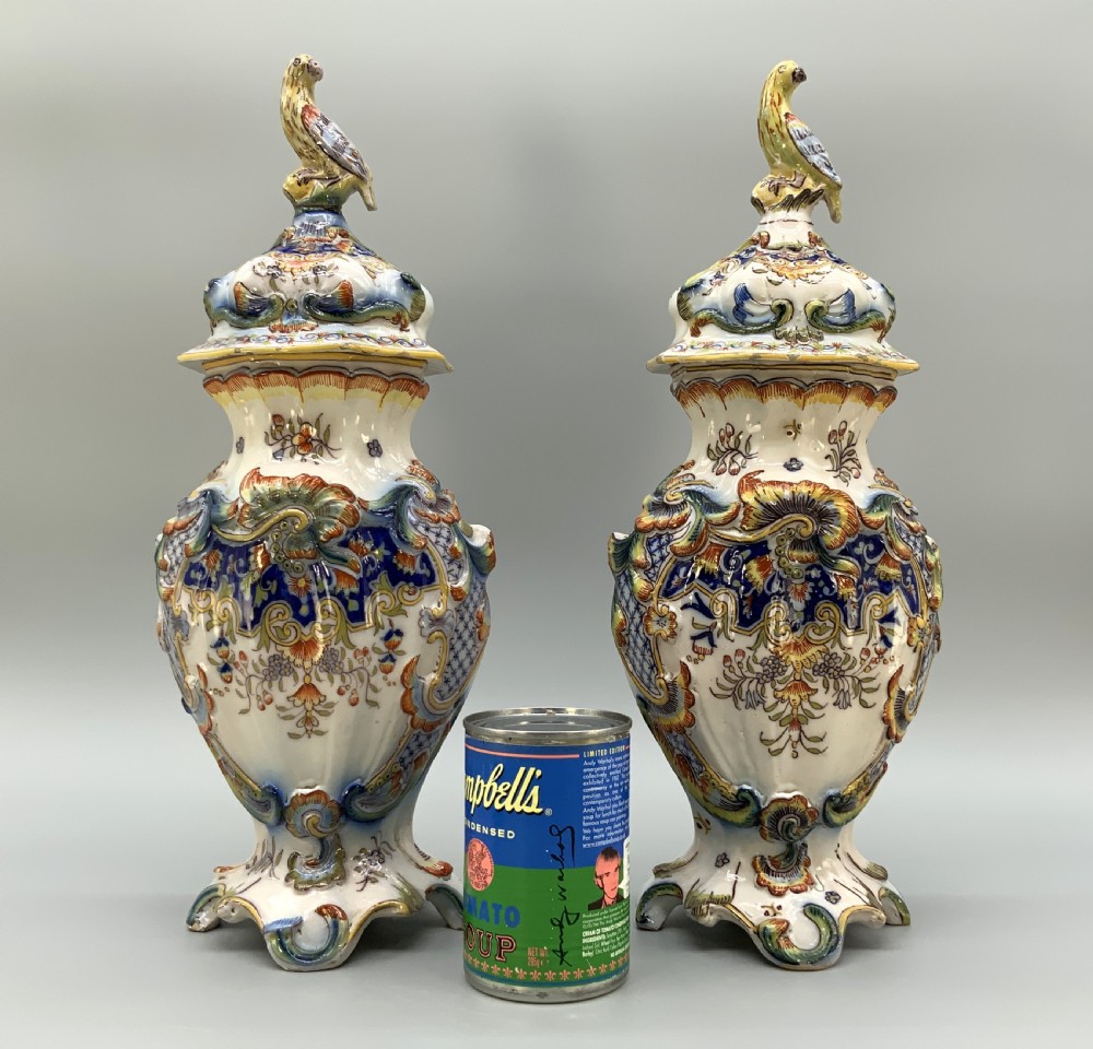 A pair of ornate French faience lidded vases decorated with hand-painted polychrome florals, Rococo scrollwork moulding, and sculptural parrot finials. View III