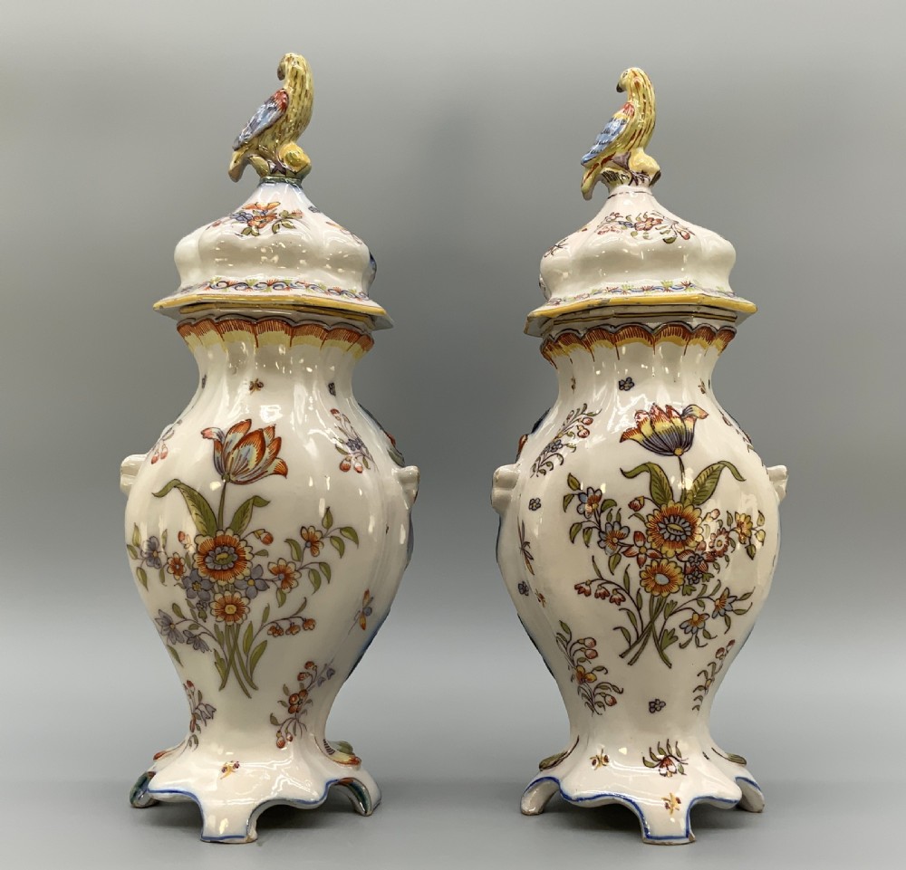 A pair of ornate French faience lidded vases decorated with hand-painted polychrome florals, Rococo scrollwork moulding, and sculptural parrot finials. View IV