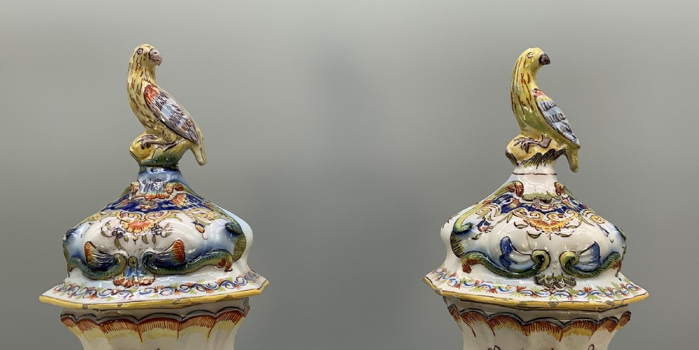A pair of ornate French faience lidded vases decorated with hand-painted polychrome florals, Rococo scrollwork moulding, and sculptural parrot finials. View VII