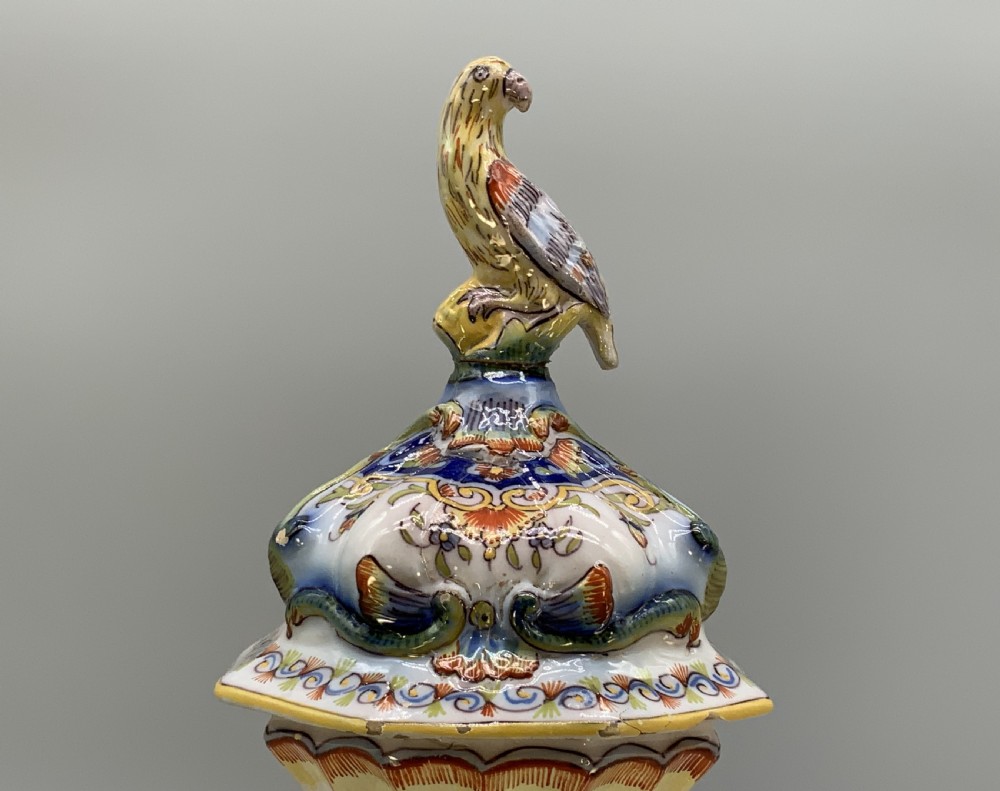 A pair of ornate French faience lidded vases decorated with hand-painted polychrome florals, Rococo scrollwork moulding, and sculptural parrot finials. View VIII