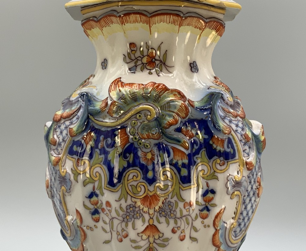 A pair of ornate French faience lidded vases decorated with hand-painted polychrome florals, Rococo scrollwork moulding, and sculptural parrot finials. View IX