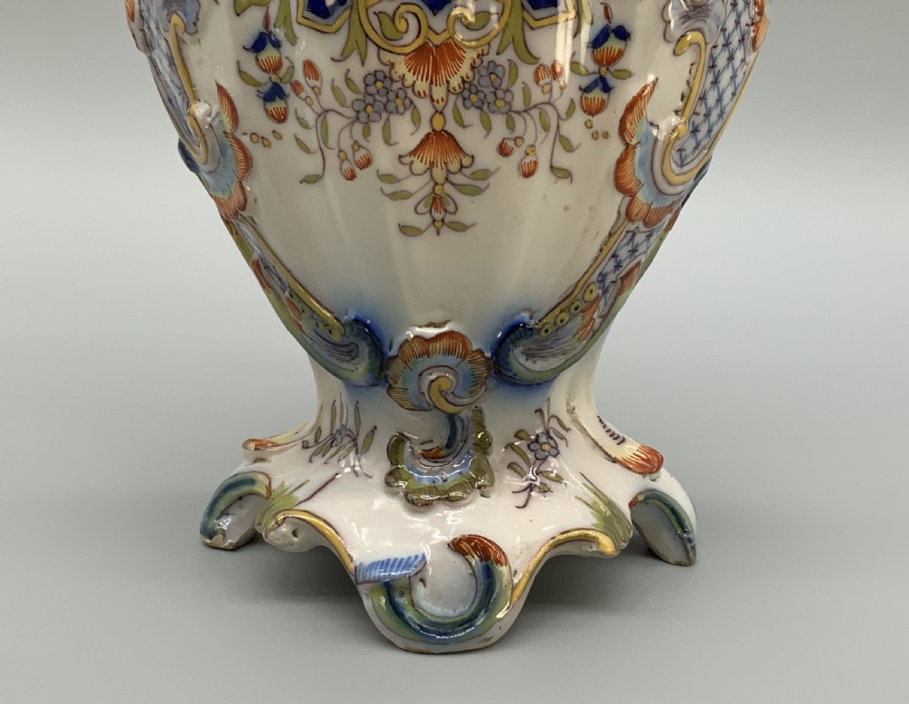 A pair of ornate French faience lidded vases decorated with hand-painted polychrome florals, Rococo scrollwork moulding, and sculptural parrot finials. View X