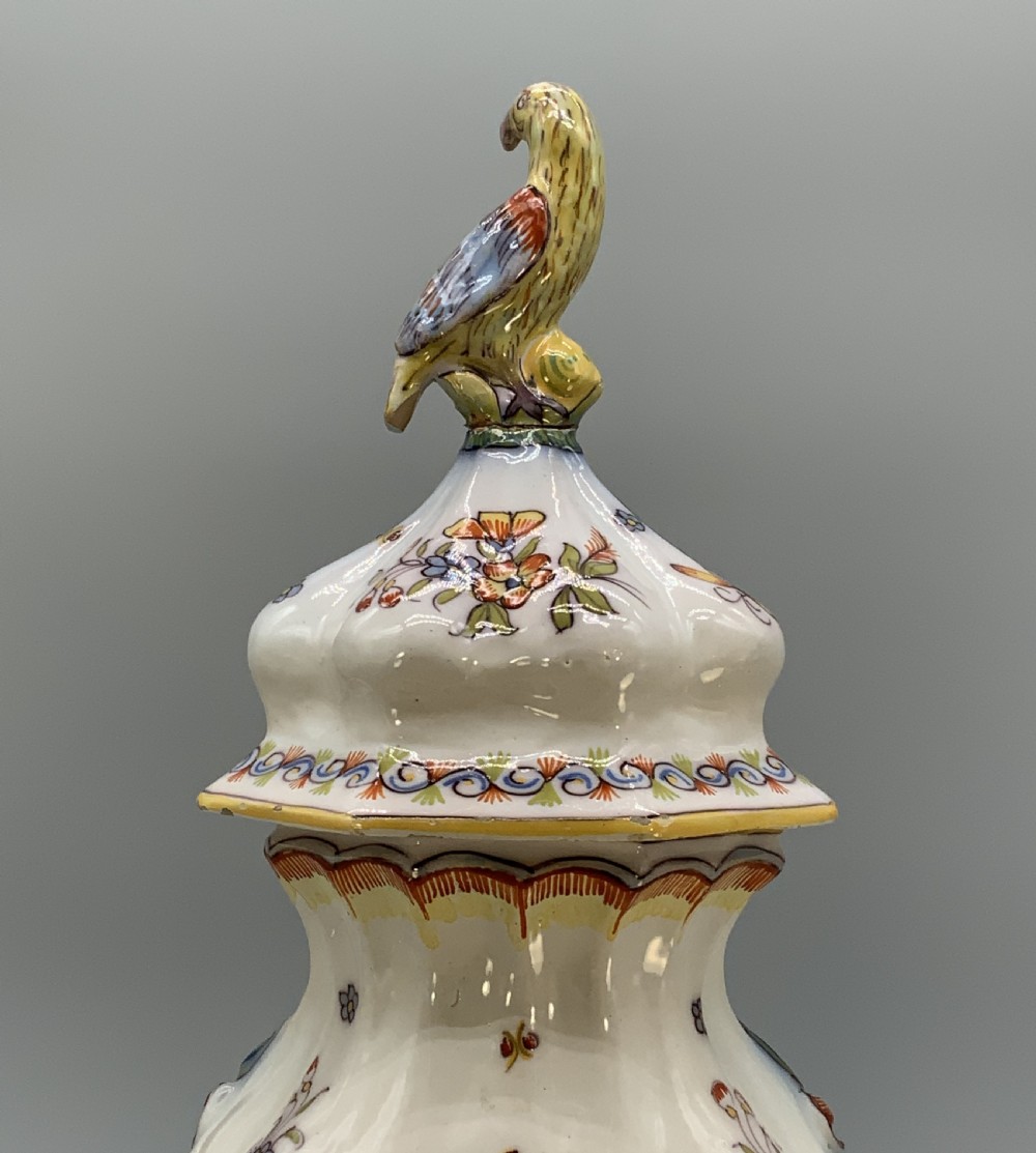 A pair of ornate French faience lidded vases decorated with hand-painted polychrome florals, Rococo scrollwork moulding, and sculptural parrot finials. View XI