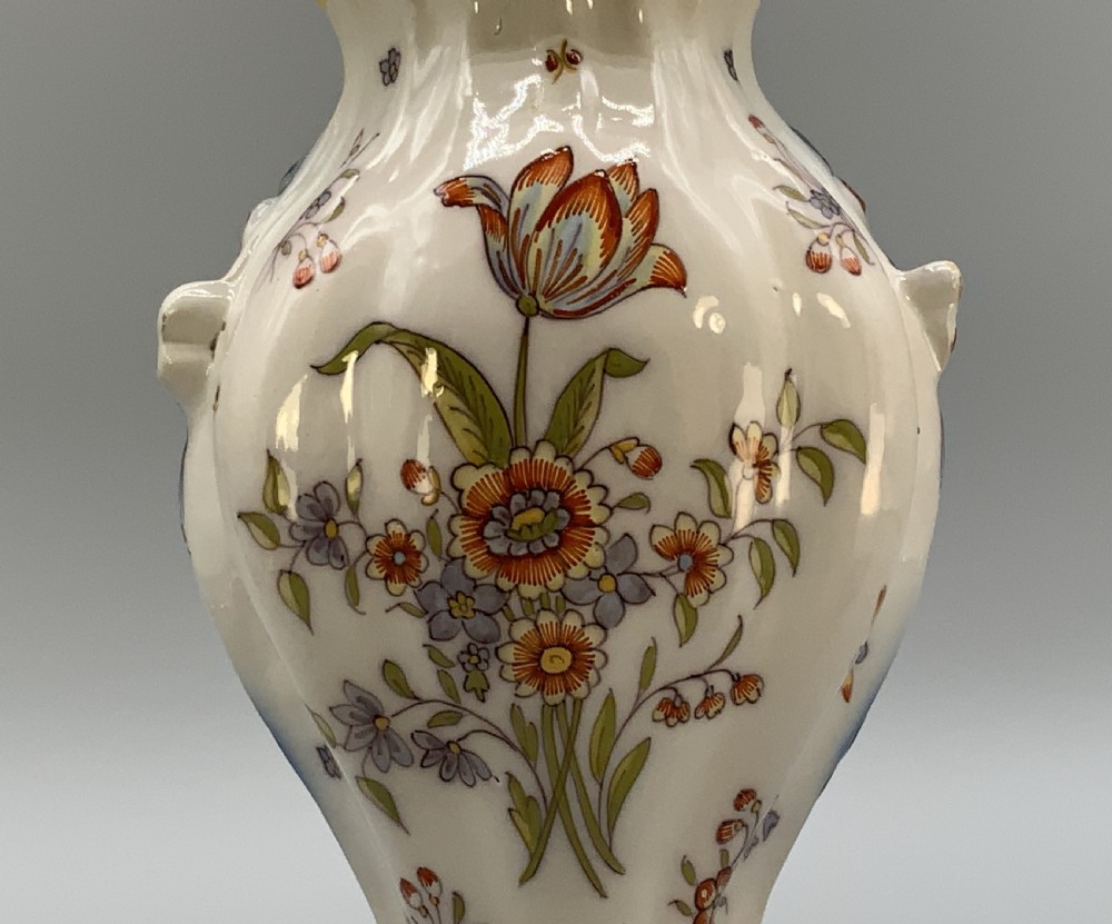 A pair of ornate French faience lidded vases decorated with hand-painted polychrome florals, Rococo scrollwork moulding, and sculptural parrot finials. View XII