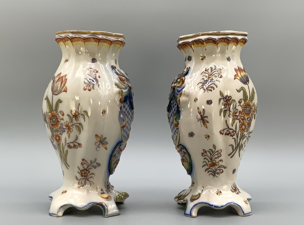 A pair of ornate French faience lidded vases decorated with hand-painted polychrome florals, Rococo scrollwork moulding, and sculptural parrot finials. View XV