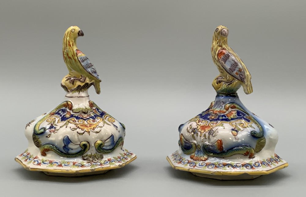 A pair of ornate French faience lidded vases decorated with hand-painted polychrome florals, Rococo scrollwork moulding, and sculptural parrot finials. View XVI