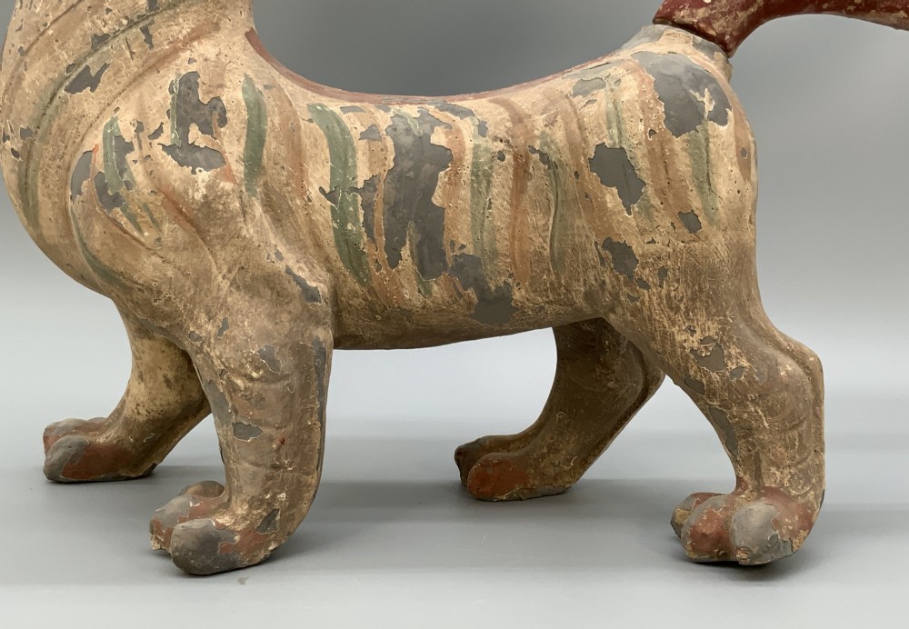 A painted earthenware figure of a tiger-like mythical beast from the Han Dynasty featuring an arched neck, raised tail, and red and green painted stripes. View VIII