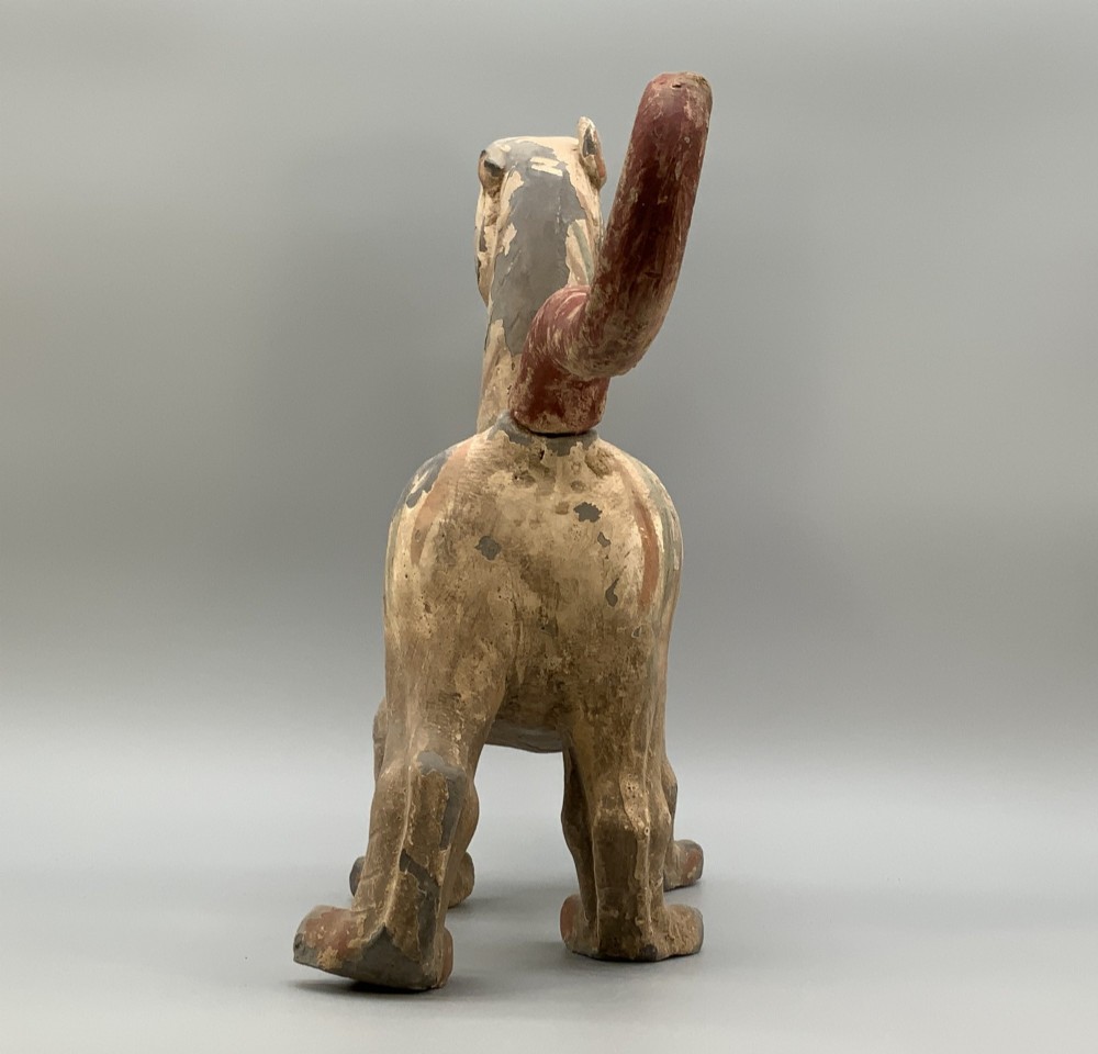 A painted earthenware figure of a tiger-like mythical beast from the Han Dynasty featuring an arched neck, raised tail, and red and green painted stripes. View XII