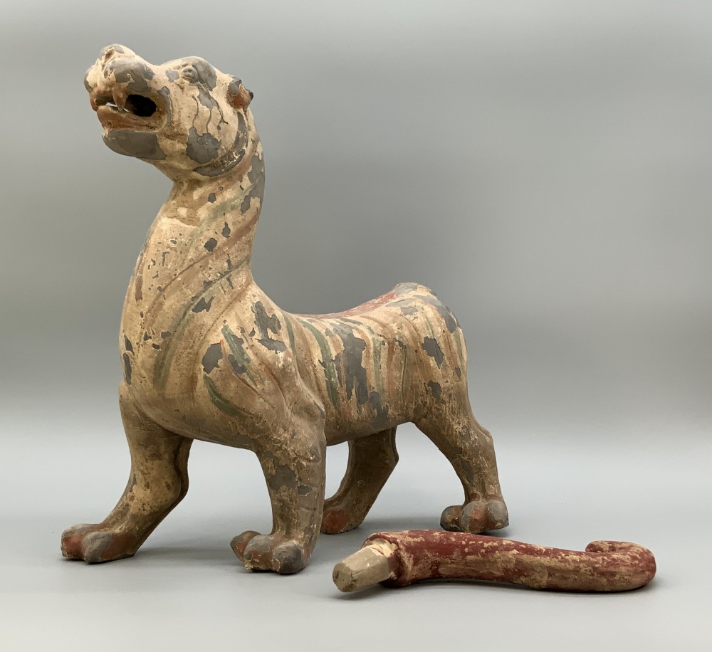 A painted earthenware figure of a tiger-like mythical beast from the Han Dynasty featuring an arched neck, raised tail, and red and green painted stripes. View XIII