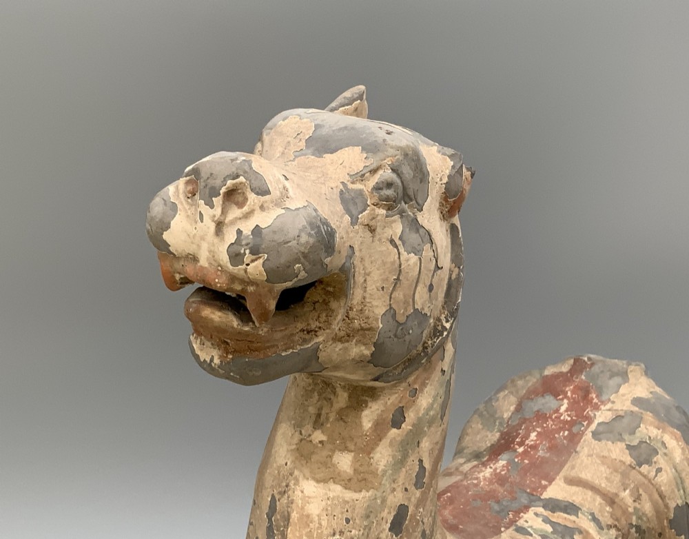 A painted earthenware figure of a tiger-like mythical beast from the Han Dynasty featuring an arched neck, raised tail, and red and green painted stripes. View XIV