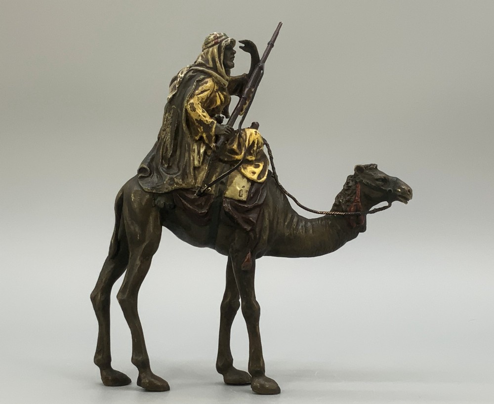 An Austrian cold-painted bronze sculpture depicting a turbaned Arab rider holding a rifle while seated atop a standing camel. View VI