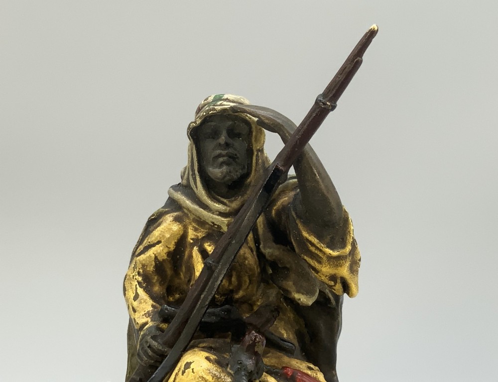 An Austrian cold-painted bronze sculpture depicting a turbaned Arab rider holding a rifle while seated atop a standing camel. View XII
