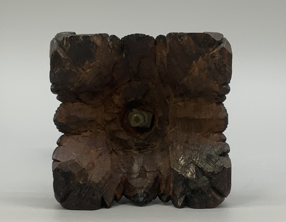 A dark patinated bronze figurine of a man carrying a log on his shoulder, mounted on an intricately carved wooden stand. View XV