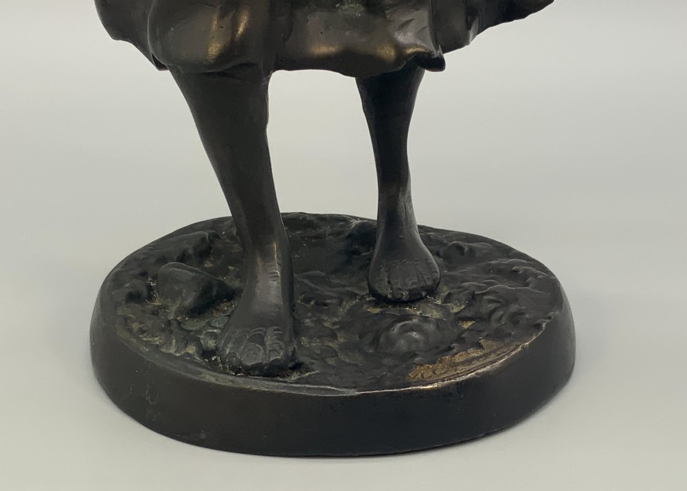 An antique dark bronze sculpture of a young maiden wearing a draped apron dress, standing barefoot on a rounded integral base. View VI