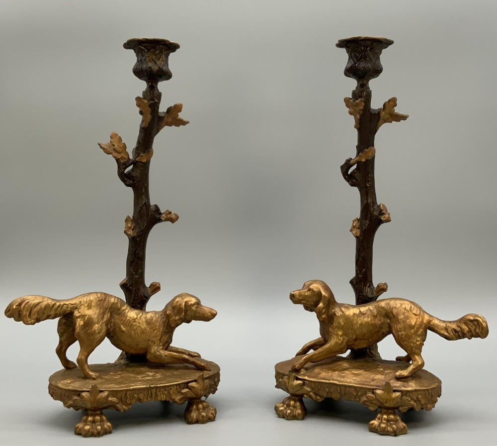 A pair of 19th-century gilded and patinated bronze candlesticks featuring detailed figures of hunting dogs at the base beneath tree-branch shafts.