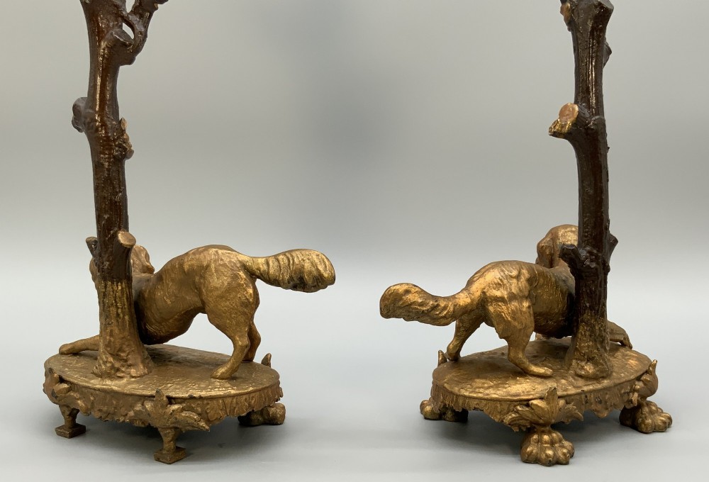 A pair of 19th-century gilded and patinated bronze candlesticks featuring detailed figures of hunting dogs at the base beneath tree-branch shafts. View VIII