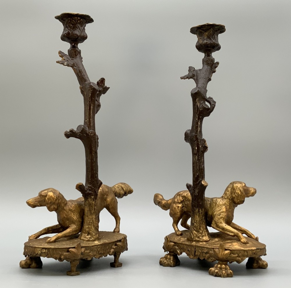 A pair of 19th-century gilded and patinated bronze candlesticks featuring detailed figures of hunting dogs at the base beneath tree-branch shafts. View X