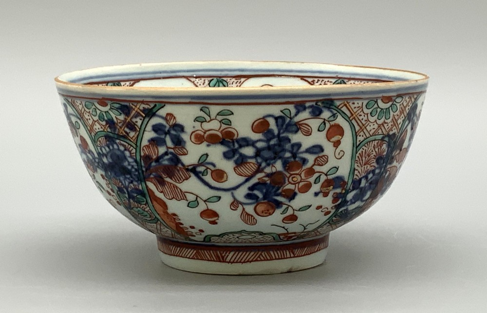 An antique deep circular porcelain bowl featuring hand-painted Chinese Imari floral foliage and diaper pattern borders in blue, red, and green.