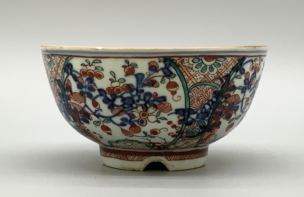 An antique deep circular porcelain bowl featuring hand-painted Chinese Imari floral foliage and diaper pattern borders in blue, red, and green. View VI