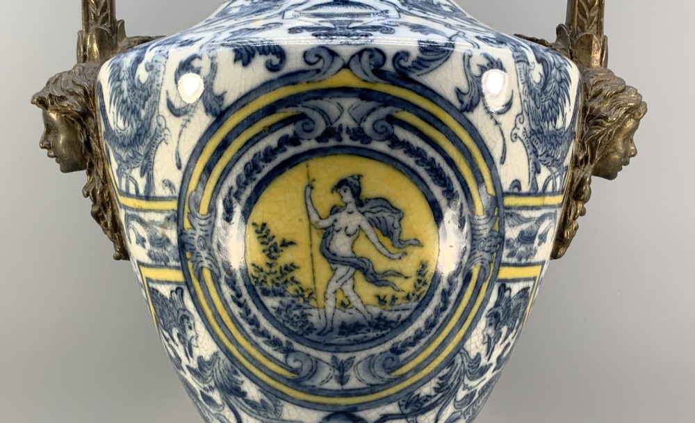 A Renaissance Revival faience vase featuring blue and yellow glazed classical medallion artwork mounted on a cast bronze footed base with mask handles. View V