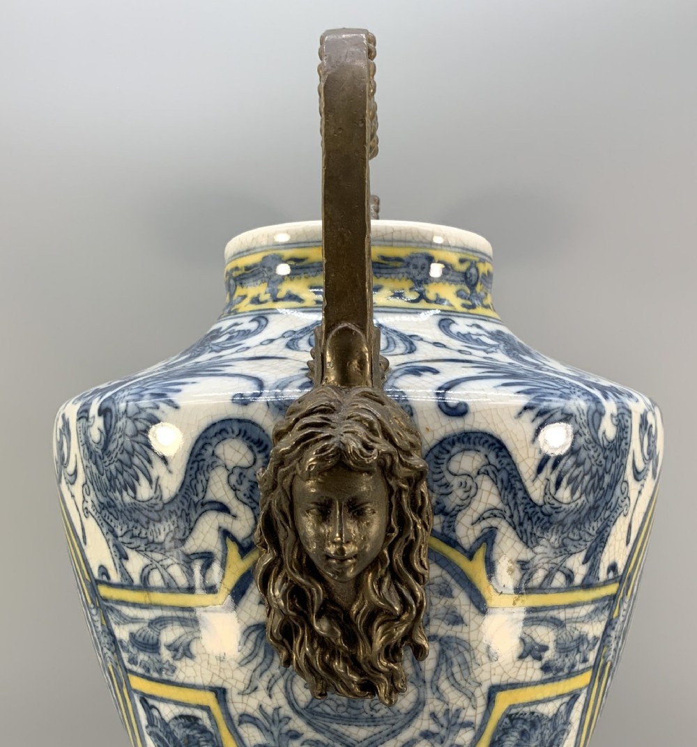 A Renaissance Revival faience vase featuring blue and yellow glazed classical medallion artwork mounted on a cast bronze footed base with mask handles. View VIII