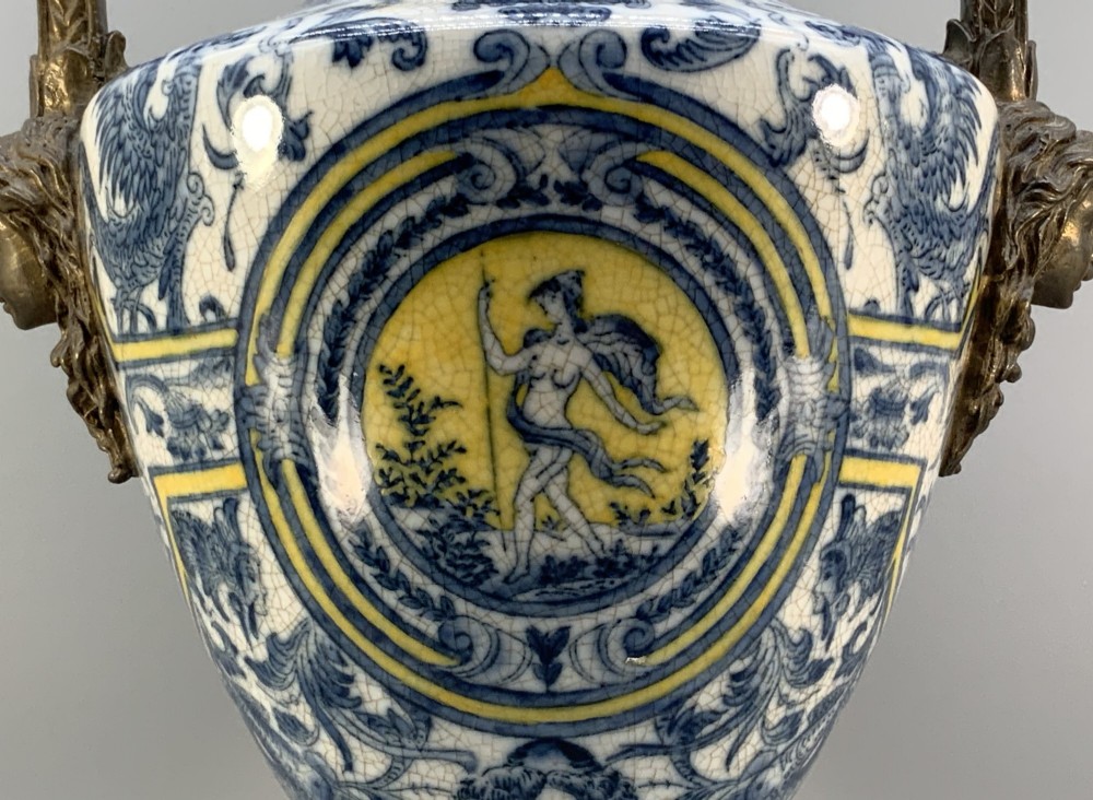 A Renaissance Revival faience vase featuring blue and yellow glazed classical medallion artwork mounted on a cast bronze footed base with mask handles. View XIV