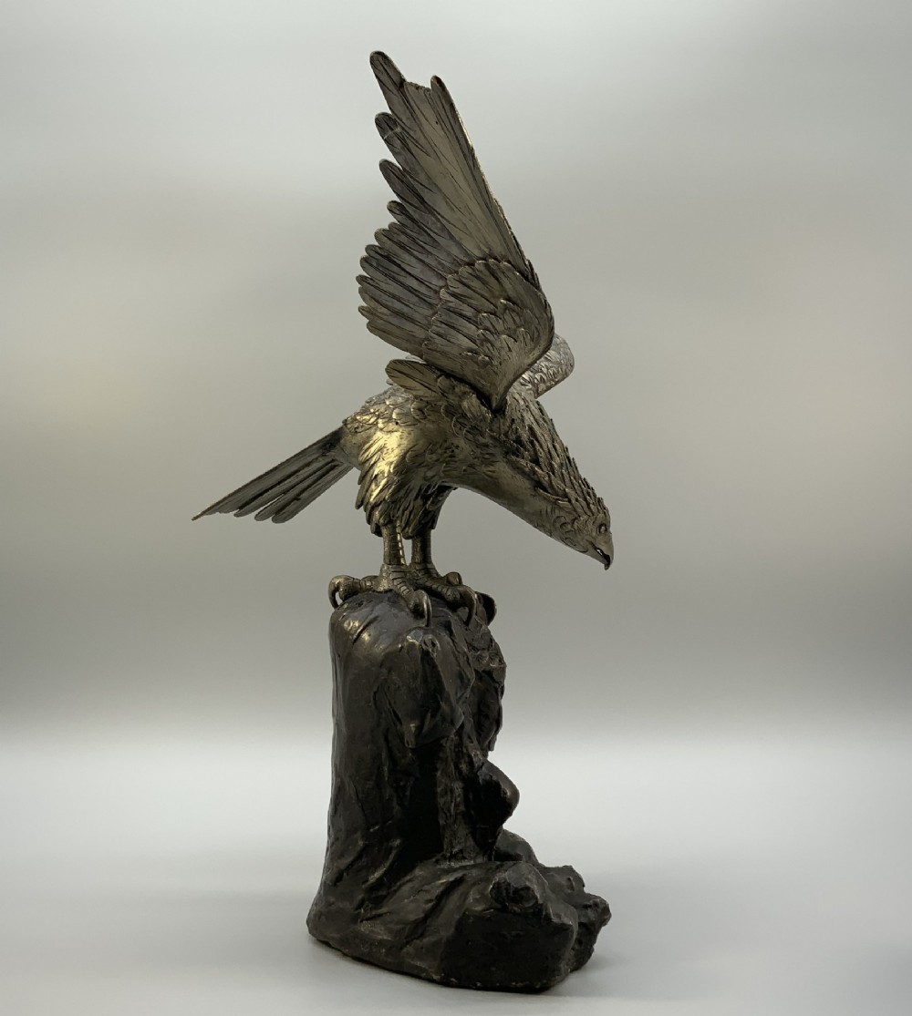 A dark bronze sculpture depicting an eagle with outstretched wings perched on a rocky base. View V