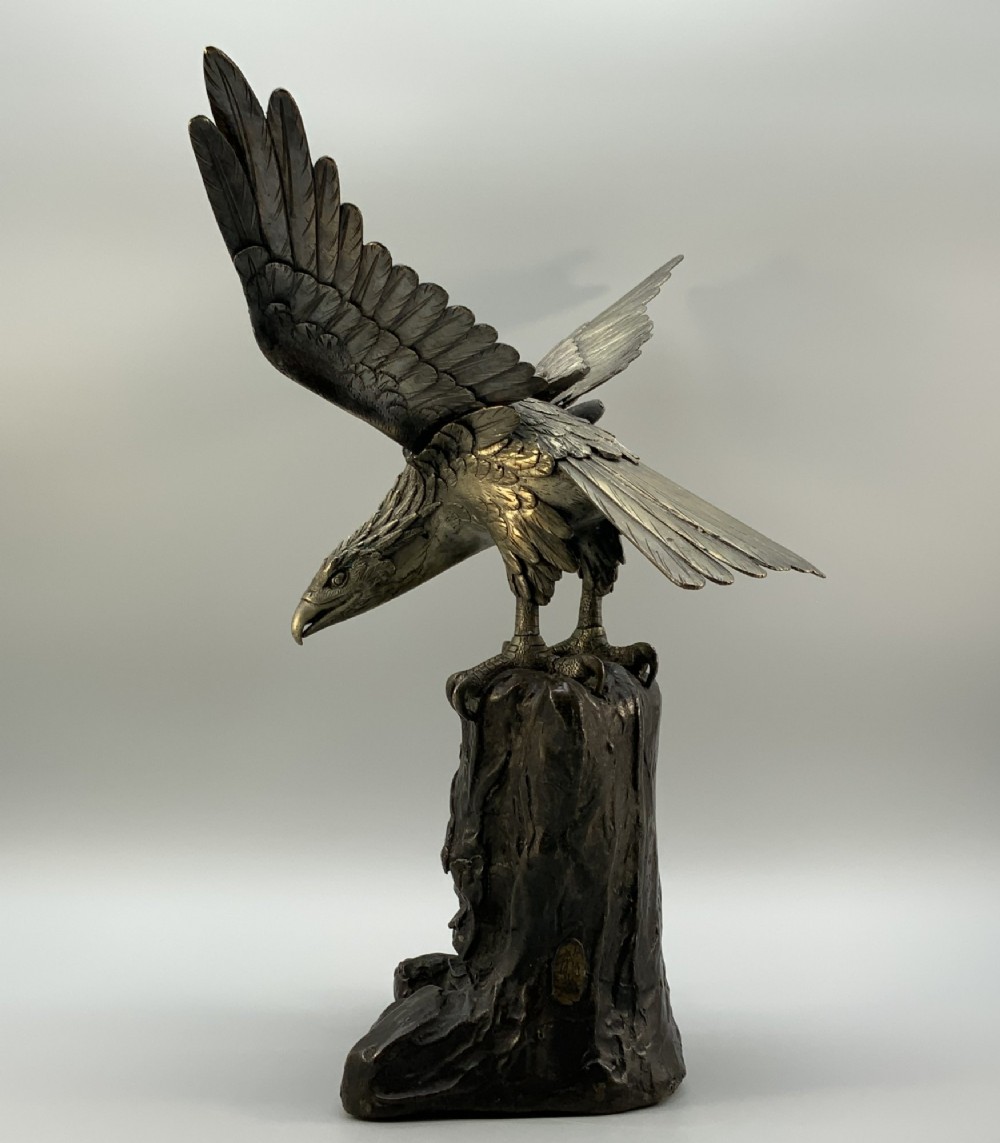 A dark bronze sculpture depicting an eagle with outstretched wings perched on a rocky base. View VII