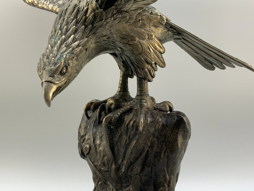 A dark bronze sculpture depicting an eagle with outstretched wings perched on a rocky base. View IX