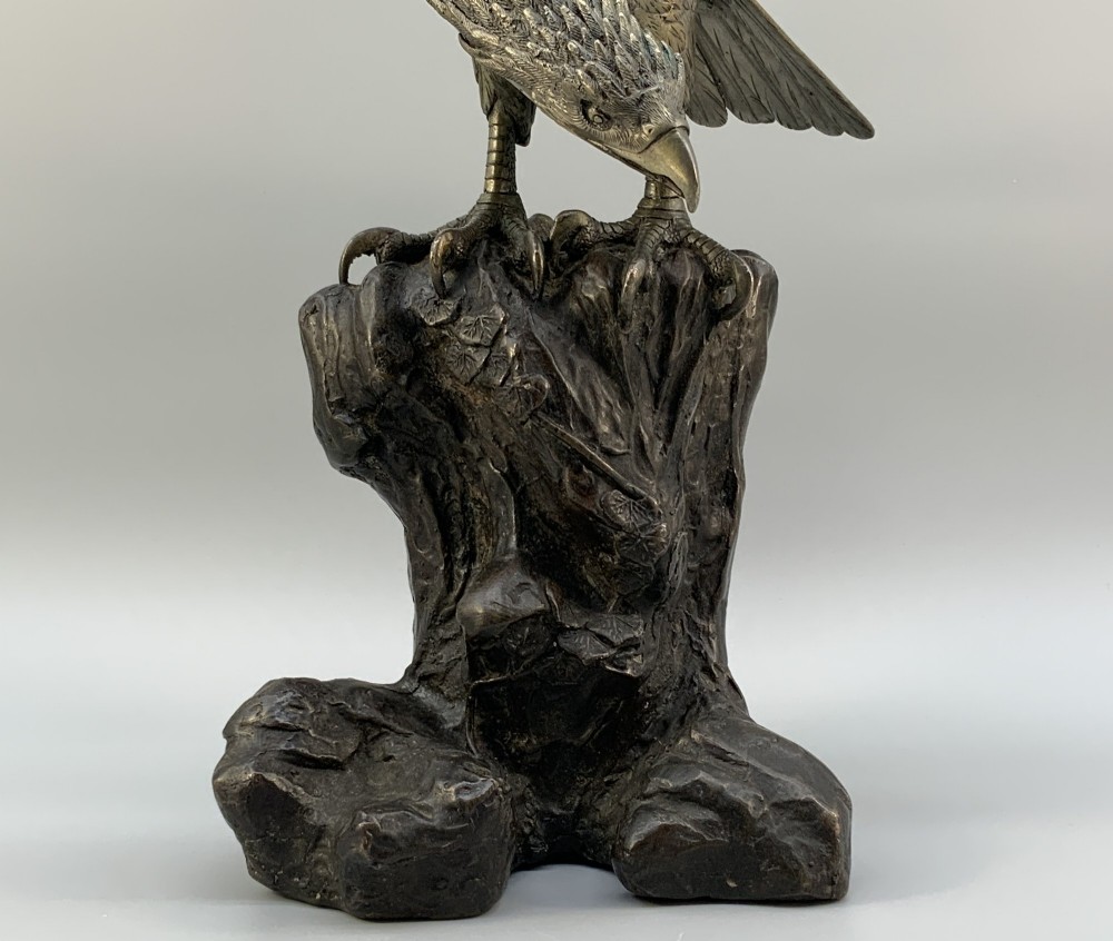 A dark bronze sculpture depicting an eagle with outstretched wings perched on a rocky base. View X