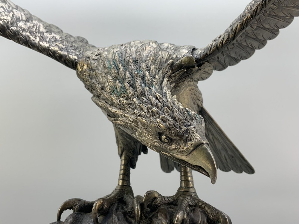 A dark bronze sculpture depicting an eagle with outstretched wings perched on a rocky base. View XV