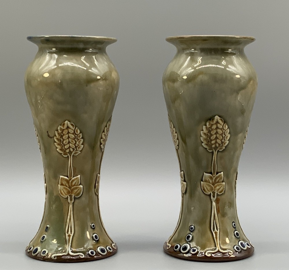 A matched pair of Royal Doulton Lambeth Art Nouveau stoneware vases featuring raised relief botanical motifs on a muted olive green glazed ground.