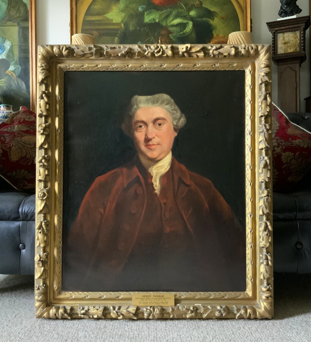 An antique oil painting depicting a half-length portrait of a gentleman in a dark red coat, set within a carved gilded frame with a metal title plaque at the bottom. View II
